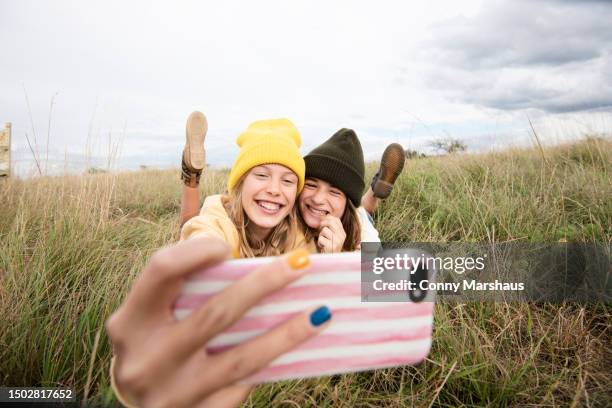 smiling girl friends lying in grass and taking selfie - happy tween girls lying on grass stock pictures, royalty-free photos & images