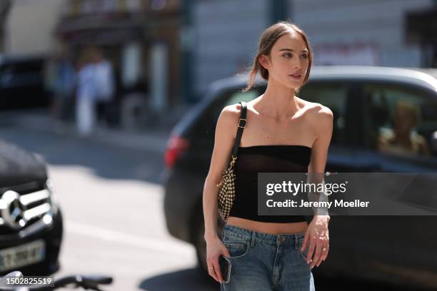 Fashion Week Guest is seen wearing strapless black top, a jeans and caro black and white bag outside during the Sacai Menswear Spring/Summer 2024 as...