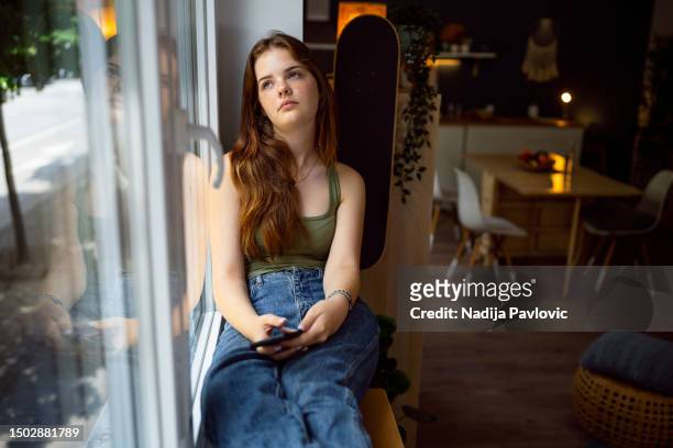 pensive caucasian teenage girl, looking through the window, while holding a mobile phone - 15 girl stock pictures, royalty-free photos & images
