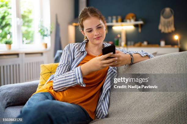 adolescente caucasico dai capelli rossi che usa il telefono cellulare mentre è seduto sul divano - girls modern room foto e immagini stock