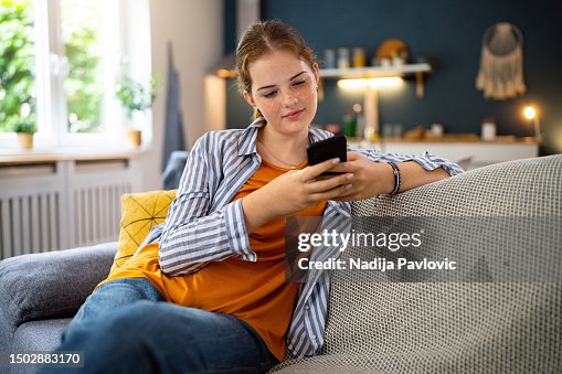 ソファに座りながら携帯電話を使う赤毛の白人の10代の少女 ソファに座りながら携帯電話を使う赤毛の白人の10代の少女