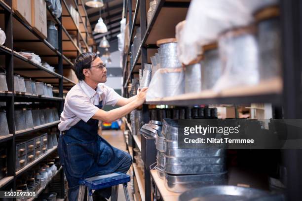 using inventory management to improve multi-channel and omnichannel performance and order fulfillment in small-business. a side view of japanese home decor employees filling a vase of aluminum on a shelf to support customer orders in a storehouse. - omnichannel retail stock pictures, royalty-free photos & images