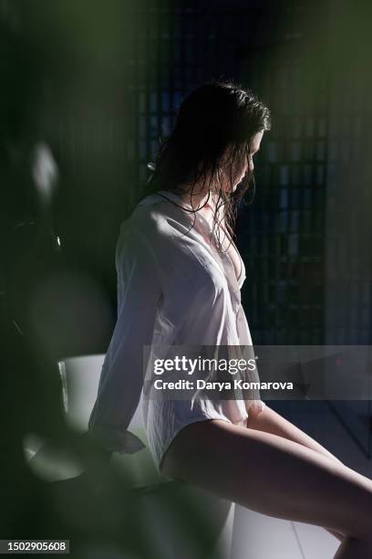 a young slender woman in a white shirt is sitting on the edge of the tub, the concept of relaxation, spa treatments, skin hydration and a modern bath room. - woman bath tub wet hair stock pictures, royalty-free photos & images