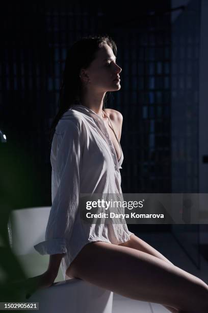 a young slender woman in a white shirt is sitting on the edge of the tub, the concept of relaxation, spa treatments, skin hydration and a modern bath room. - woman bath tub wet hair stock pictures, royalty-free photos & images