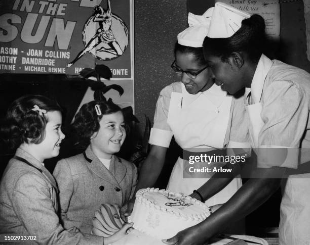 Twin sisters Rosiland and Susan Mitchell present a cake to Vincentian nurse Pamila John and Barbadian nurse Olga Worrell, both on the staff at...