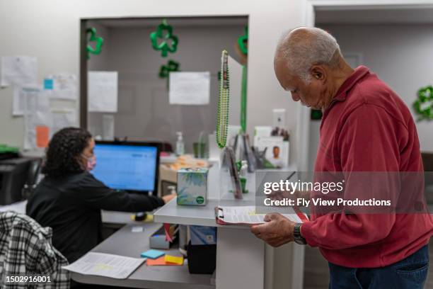 senior man completing paperwork at medical appointment - medicaid stock pictures, royalty-free photos & images