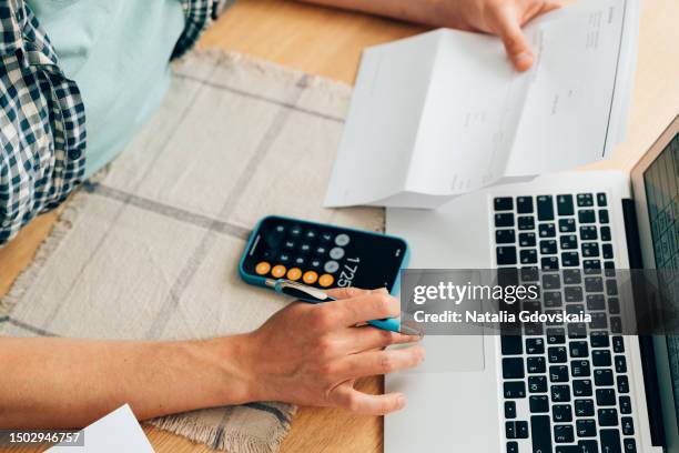 unrecognizable person counting expenses on calculator in mobile phone app, checking her energy bills at home. budget management, price increases, inflation, rise in price of products and utilities. view from above, managing home finances - high rise film stock-fotos und bilder