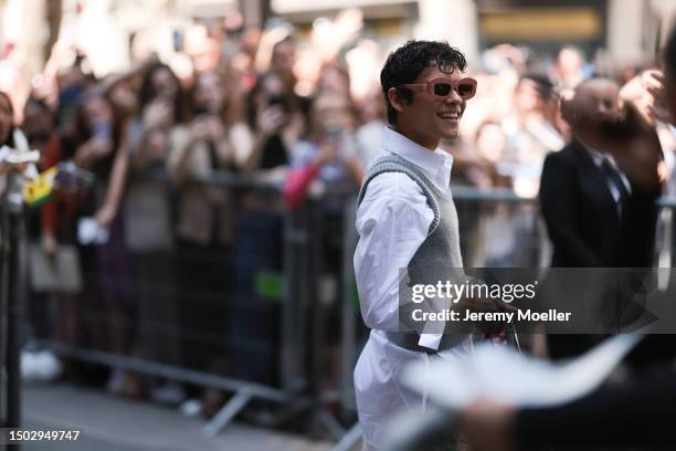 Omar Rudberg is seen wearing red and rosa colored shades, an oversized white shirt with a big collar, above a grey sleeveless pullover, a silver ring...