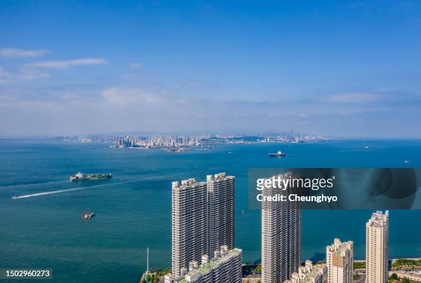 two large cargo ship in front of qingdao city skyline, shandong province, china - qingdao photos et images de collection