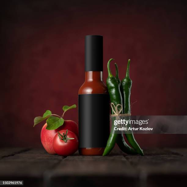 bottle of chili ketchup with peppers, tomato and apple on table. spicy ketchup in glass jar. green chili pods. spicy food. wooden table. burgundy background. front view. copy space - scharfe sauce stock-fotos und bilder