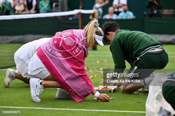 Australia's Daria Saville and Britain's Katie Boulter help ball boys and girls to pick up orange confetti thrown on court 18 by a Just Stop Oil...