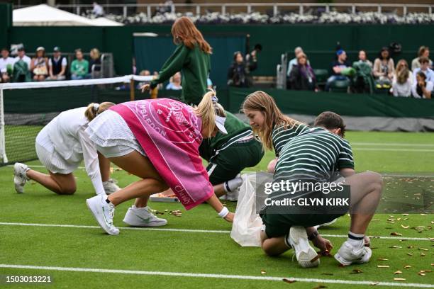 Australia's Daria Saville and Britain's Katie Boulter help ball boys and girls to pick up orange confetti thrown on court 18 by a Just Stop Oil...