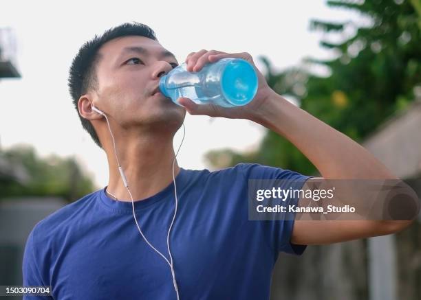 fitter junger asiatischer mann, der aus wasserflasche trinkt - mann wasser trinken sport stock-fotos und bilder