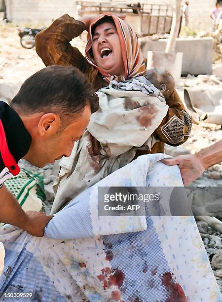 Syrian woman holds her dead baby as she screams upon seeing her husband's body being covered following an airstrick by regime forces on the town of...