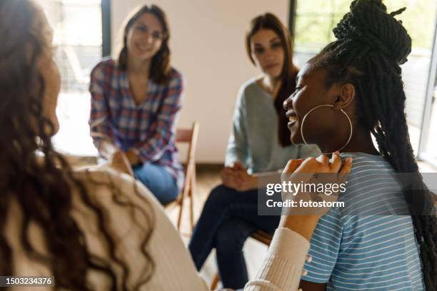 compassionate young woman holding hand on friend's shoulder during a group therapy session - group therapy stock pictures, royalty-free photos & images