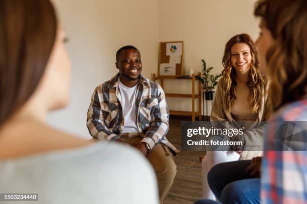 jóvenes riendo mientras conversan casualmente durante una sesión de terapia grupal - terapia de grupo fotografías e imágenes de stock