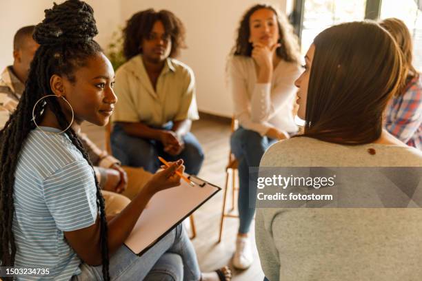 female therapist writing notes during a group therapy session - terapia-de-grupo imagens e fotografias de stock
