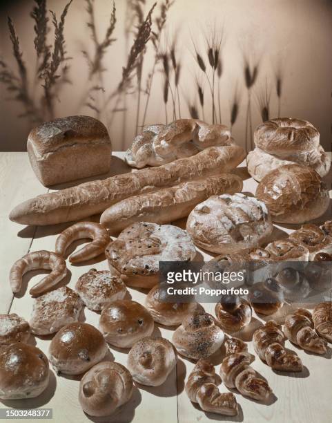 Close up studio display of home made bread and bakery products, including farmhouse loaves, a sandwich loaf, baguettes, current buns, poppy seed...