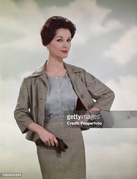 Posed studio portrait of a female fashion model wearing a blue-grey button up blouse under a matching pencil skirt and short jacket in Prince of...