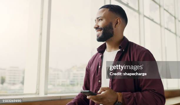 telefon, fenster und aussicht mit einem geschäftsmann im büro, der über die zukunft der kommunikation nachdenkt. idee, lächeln und stadtbild mit einem glücklichen jungen männlichen mitarbeiter, der am arbeitsplatz eine textnachricht tippt - happy smile with phone stock-fotos und bilder