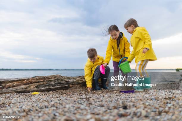 happy three children playing together at pebble beach, near the sea. - gummistiefel stock-fotos und bilder