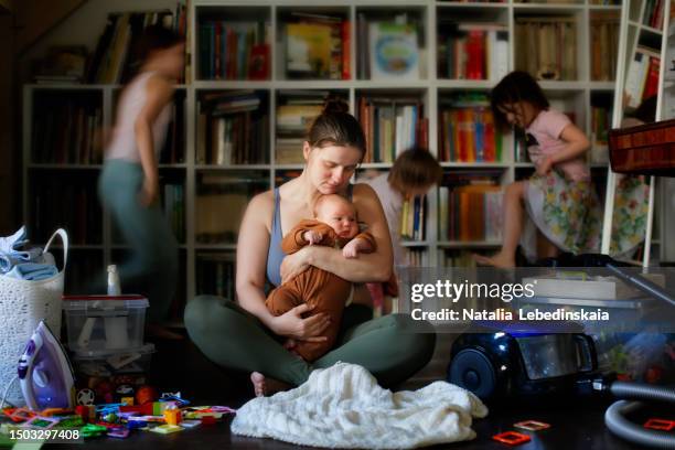 capturing emotions: tired mother's desperation with baby in arms, unfocused kids, and household chaos in the living room - stressed parent stock pictures, royalty-free photos & images