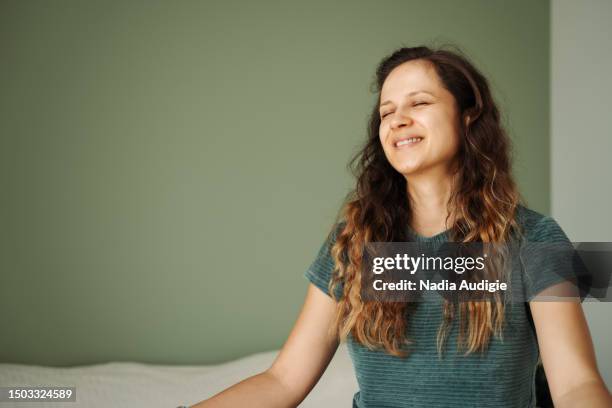 woman sitting cross legged on a bed with closed eyes - no make up stockfoto's en -beelden