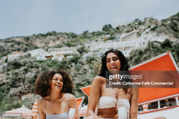 two woman on sun loungers drink champagne on a beach - costiera amalfitana foto e immagini stock