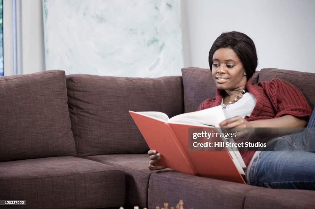Black woman reading book on sofa