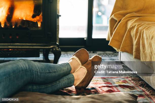 feet in brown slippers near the fireplace in the house. - chinelo imagens e fotografias de stock