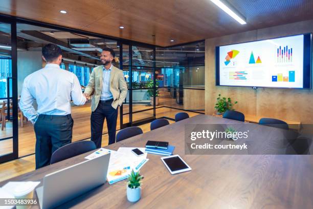 geschäftsmänner händedruck in einem sitzungssaal. es gibt eine whiteboard-präsentation mit finanzdatendiagrammen - presentation to customers stock-fotos und bilder