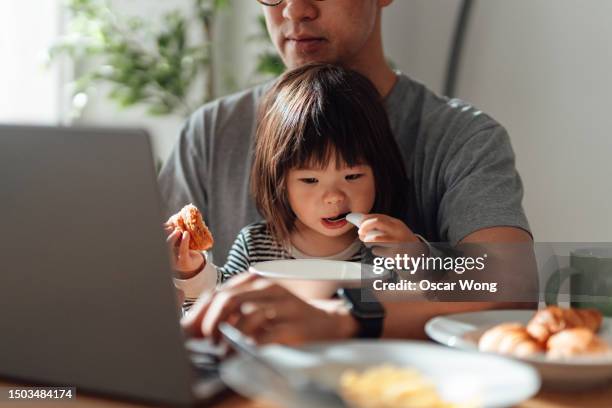 cropped hot of young asian father taking care of his little daughter while working from home with laptop - real family stock pictures, royalty-free photos & images