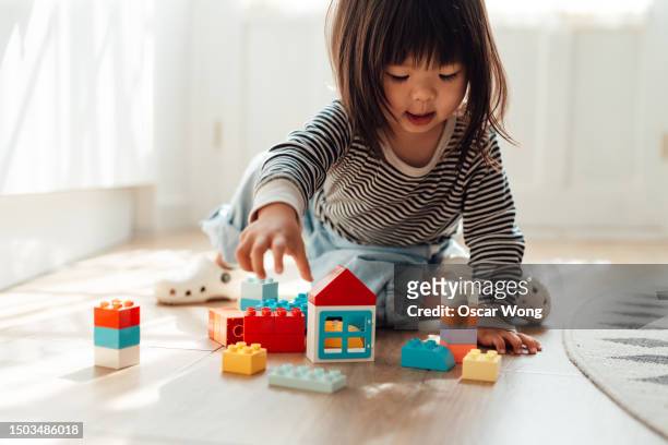 cheerful little asian girl playing toy blocks in living room at home - china games day 1 fotografías e imágenes de stock