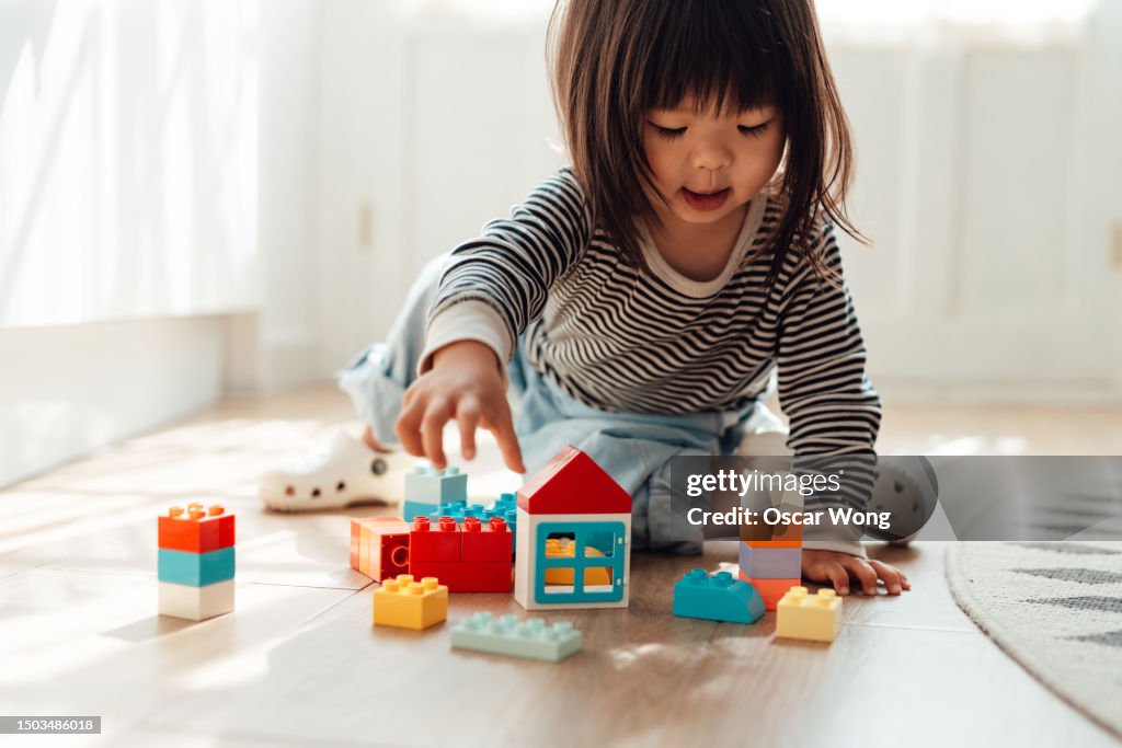 Cheerful little Asian girl playing toy blocks in living room at home