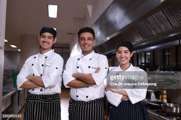 portrait cooks with modern kitchen background, smiling cooks looking at the camera. cooking, culinary and professional concept - an international team of smiling chefs with crossed arms - chef team stock pictures, royalty-free photos & images
