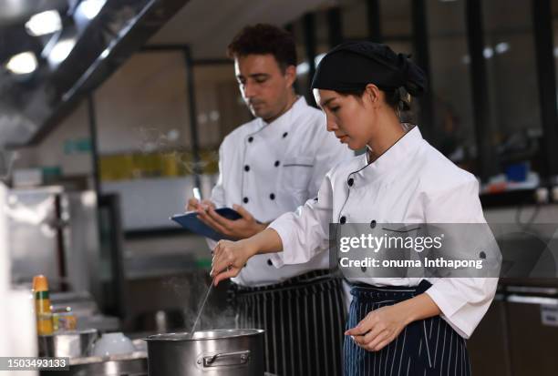 köchin bringt dem schüler bei, wie man suppe kocht, eine köchin in der küche bietet ihren schülern kochtraining an. männliche kochlehrlinge schauen und kochen gerne zusammen. köche, die eine kochuniform tragen. sehen sie appetitlich aus. - kochlehrling stock-fotos und bilder