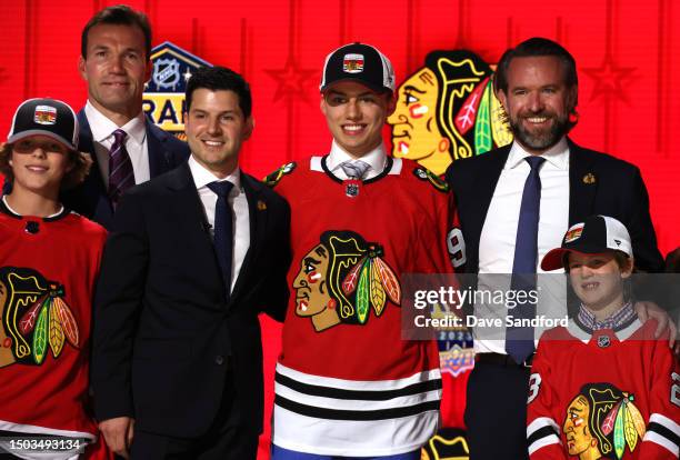 Connor Bedard stands onstage with team personnel after being selected first overall by the Chicago Blackhawks during the 2023 Upper Deck NHL Draft -...
