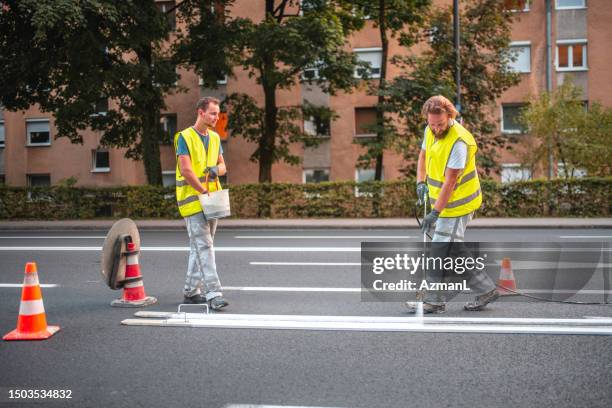 mid adult male road maintenance workers spray painting the road - road construction crew stock pictures, royalty-free photos & images
