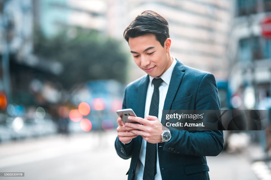 Well-Dressed Young Male Chinese Corporate Employee Using A Smart Phone Outdoors