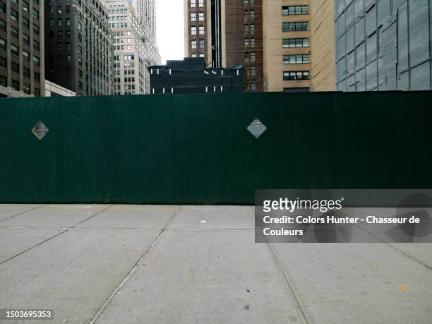 a construction fence made of green wood panels on a cement sidewalk and in front of buildings in manhattan, new york state, united states - pavement stockfoto's en -beelden