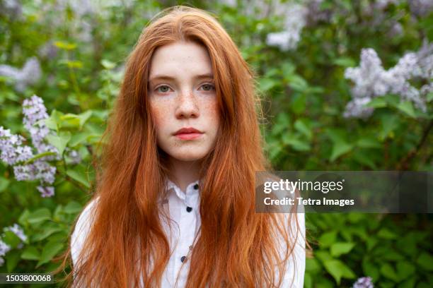 portrait of serious teenage girl (16-17) against lilac bush - ginger bush stock pictures, royalty-free photos & images