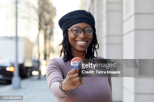 Portrait of smiling woman showing Vote button in city