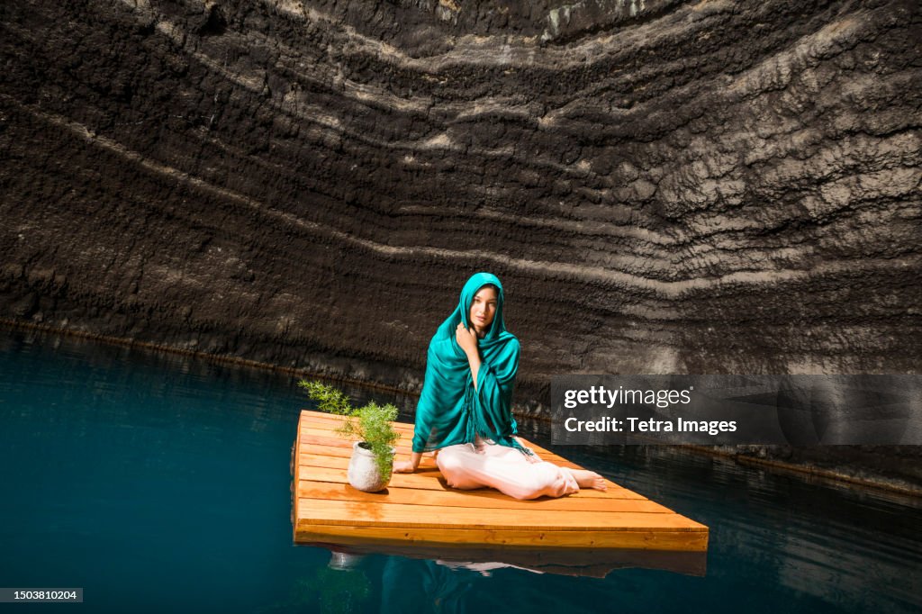 Portrait of woman sitting on floating dock near rocky coast
