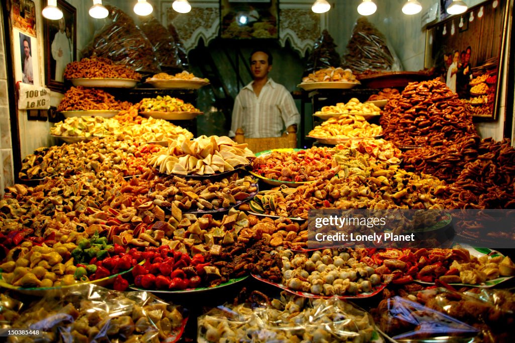 Vendor surrounded by piles of sweets in souk stall.