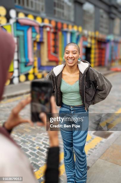 friend photographing young woman on city street - shoreditch stock pictures, royalty-free photos & images