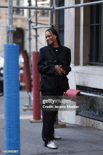 Guest is seen wearing black sunglasses, a black shiny suit with big attached bags and zippers on the blazer combined with black Botter shirt with...