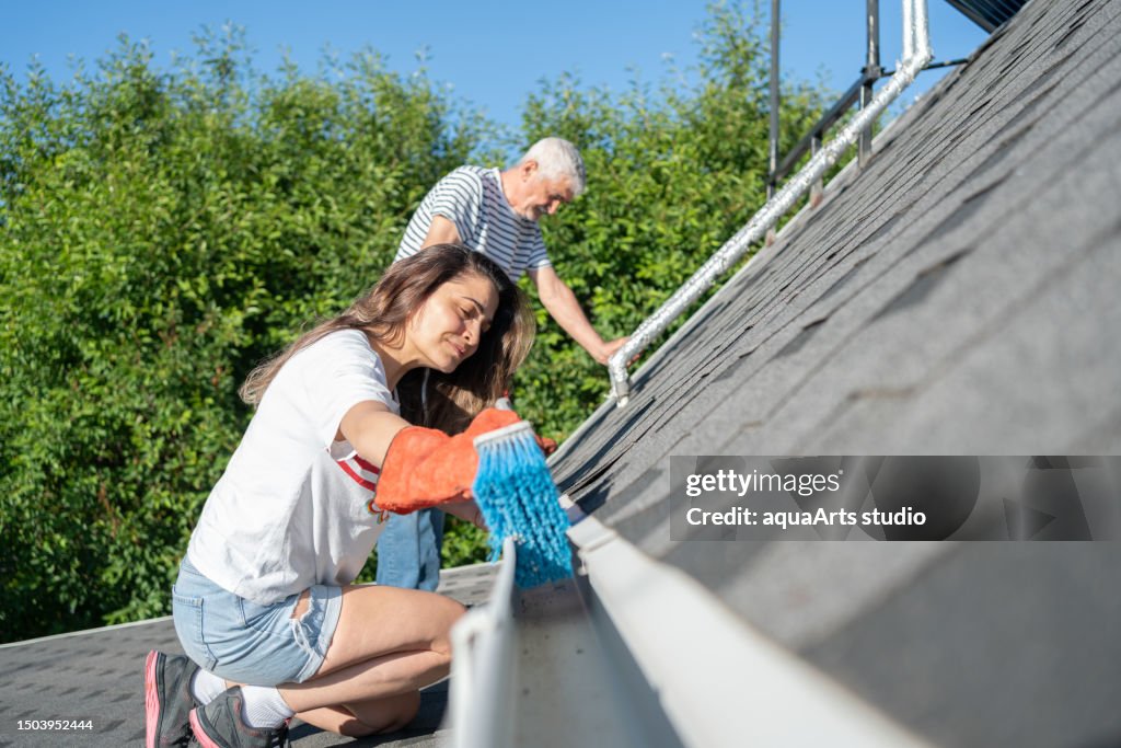 Senior Man And Woman Cleaning Their House Roof Gutters