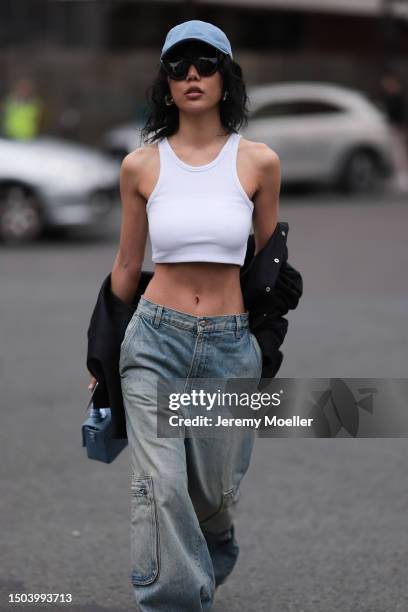 Xiayan Guo is wearing a denim blue cap from Lovechild 1979, large black sunglasses, a cropped white tank top, wide low waist denim pants in used...