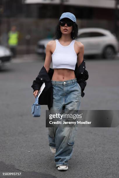 Xiayan Guo is wearing a denim blue cap from Lovechild 1979, large black sunglasses, a cropped white tank top, wide low waist denim pants in used...