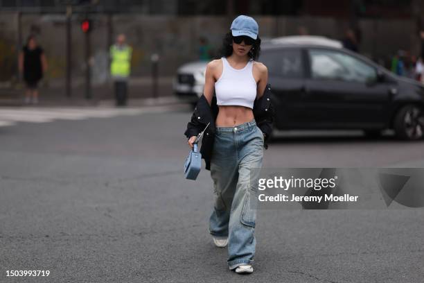 Xiayan Guo is wearing a denim blue cap from Lovechild 1979, large black sunglasses, a cropped white tank top, wide low waist denim pants in used...